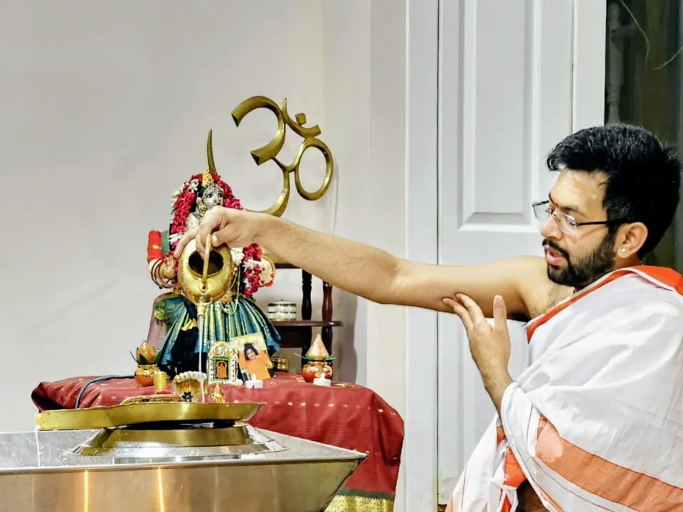 Purohit Surya performing abhishekam over a Shiva Lingam at a home altar